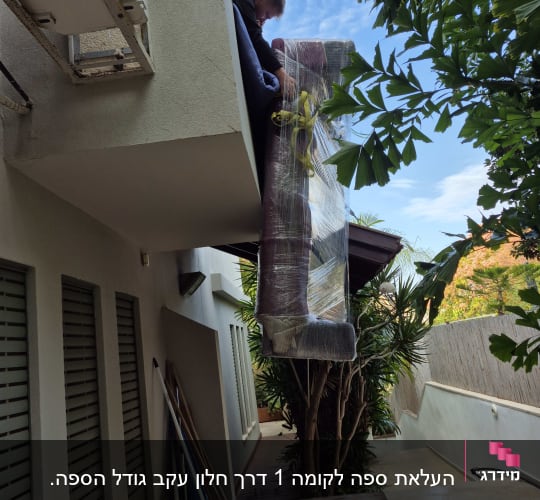 אדם מוריד ספה עטופה מהמרפסת בעזרת רצועות